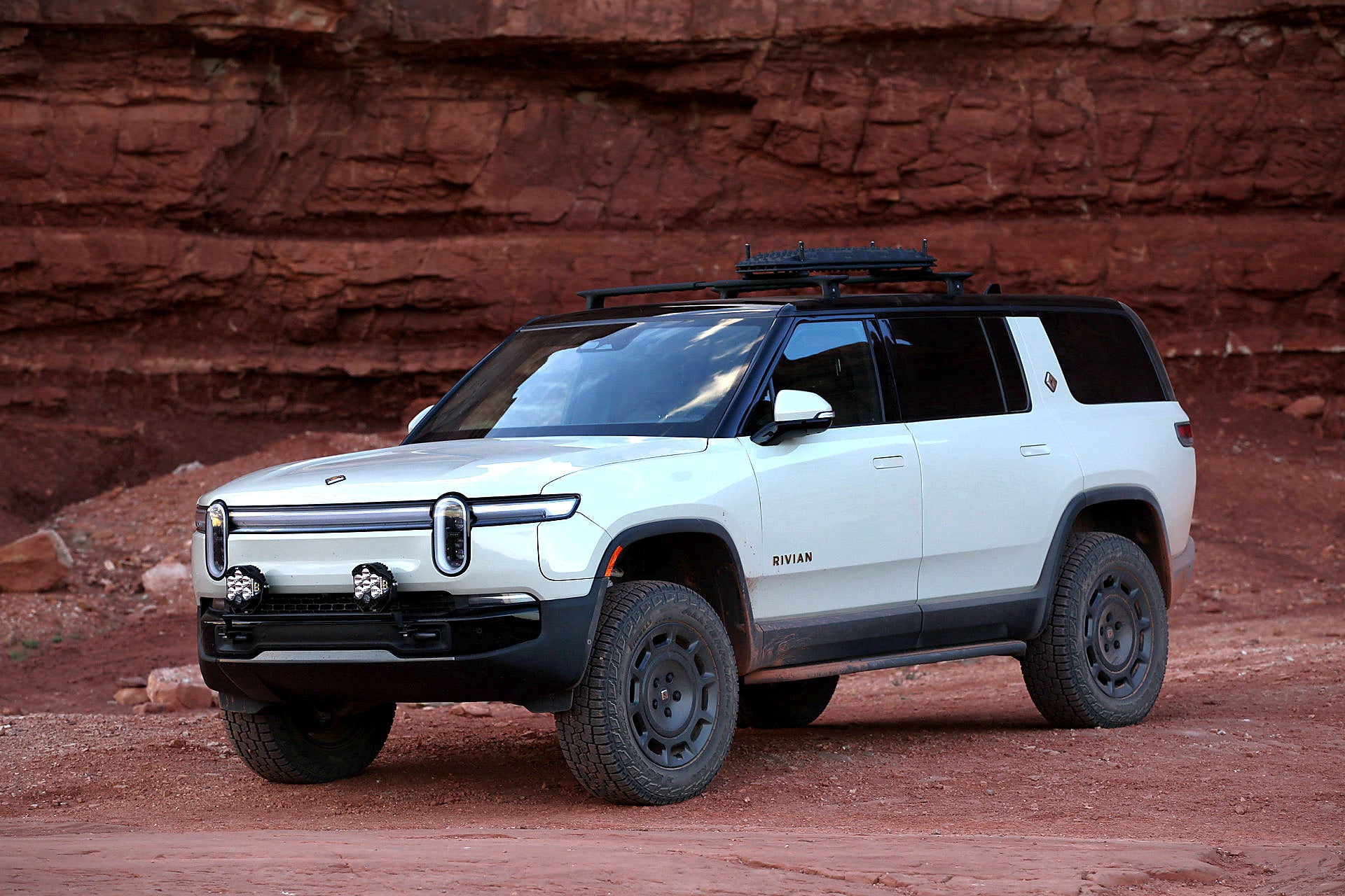 White Rivian R1S with an Elevation EV light rail and Baja Designs lights beneath red sandstone cliffs